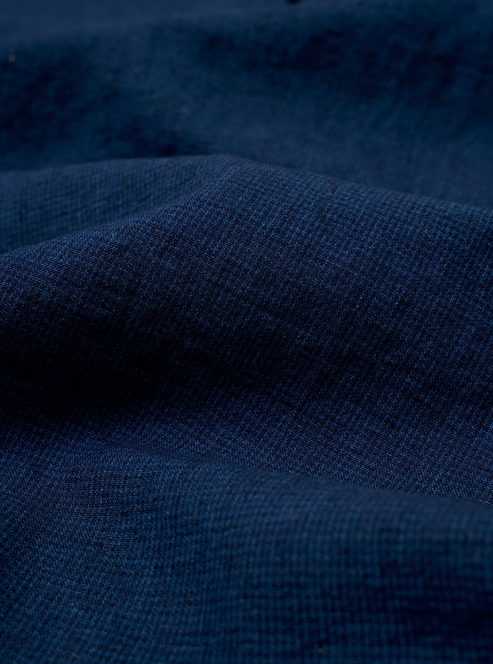 A close-up fabric swatch of the Indigo Lincot Denim Lazy Day Shirt highlights the rich indigo blue color and the distinct diagonal weave of the cotton-linen denim. The image provides a detailed view of the textile's texture and color variations.
