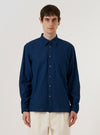A model wears the Indigo Lincot Denim Lazy Day Shirt against a plain, neutral background. The shirt features a button-down front, a pointed collar, and a single patch pocket on the chest. The garment is made from a deep indigo denim fabric with a visible texture.