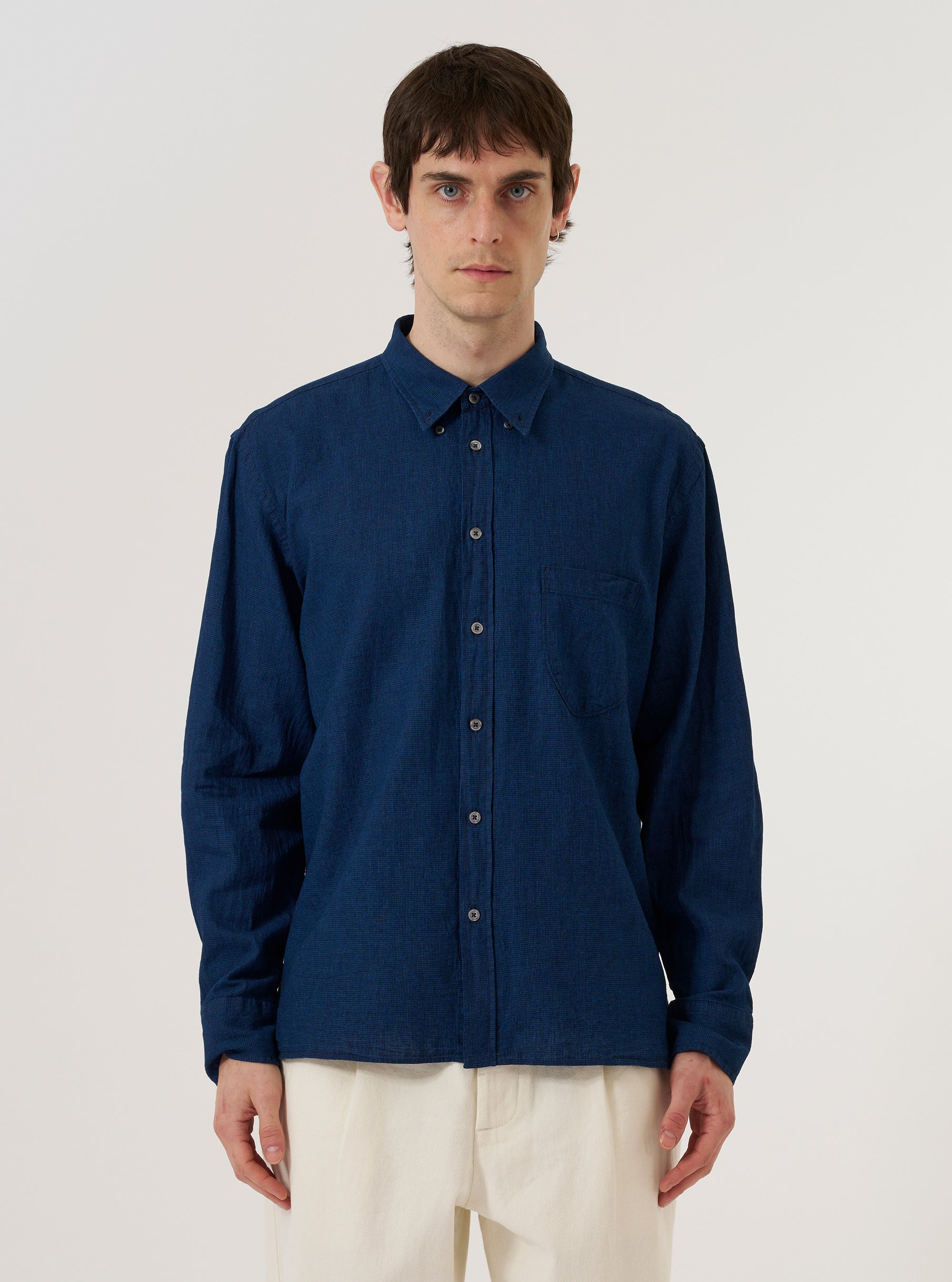 A model wears the Indigo Lincot Denim Lazy Day Shirt against a plain, neutral background. The shirt features a button-down front, a pointed collar, and a single patch pocket on the chest. The garment is made from a deep indigo denim fabric with a visible texture.