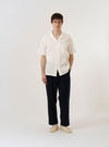 The Ecru Arten Seersucker Road Shirt is shown as a flat lay against a plain white background. The short-sleeve shirt features a camp collar with a loop-button closure at the neck, a central button-down front, and a single patch pocket on the left chest. The ecru-colored organic cotton fabric has a distinct puckered seersucker texture.