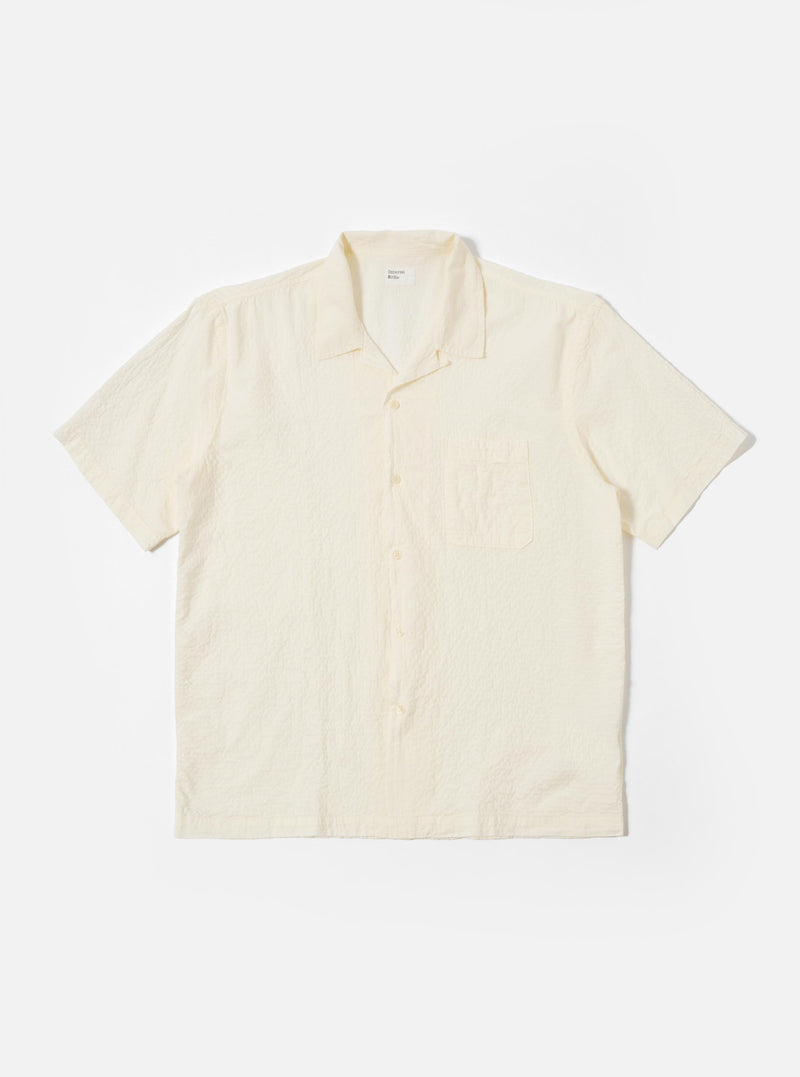 The Ecru Arten Seersucker Road Shirt is shown as a flat lay against a plain white background. The short-sleeve shirt features a camp collar with a loop-close button detail, a central button-down front, a single chest patch pocket, and a straight hem. The ecru-colored fabric has a distinct puckered seersucker texture.