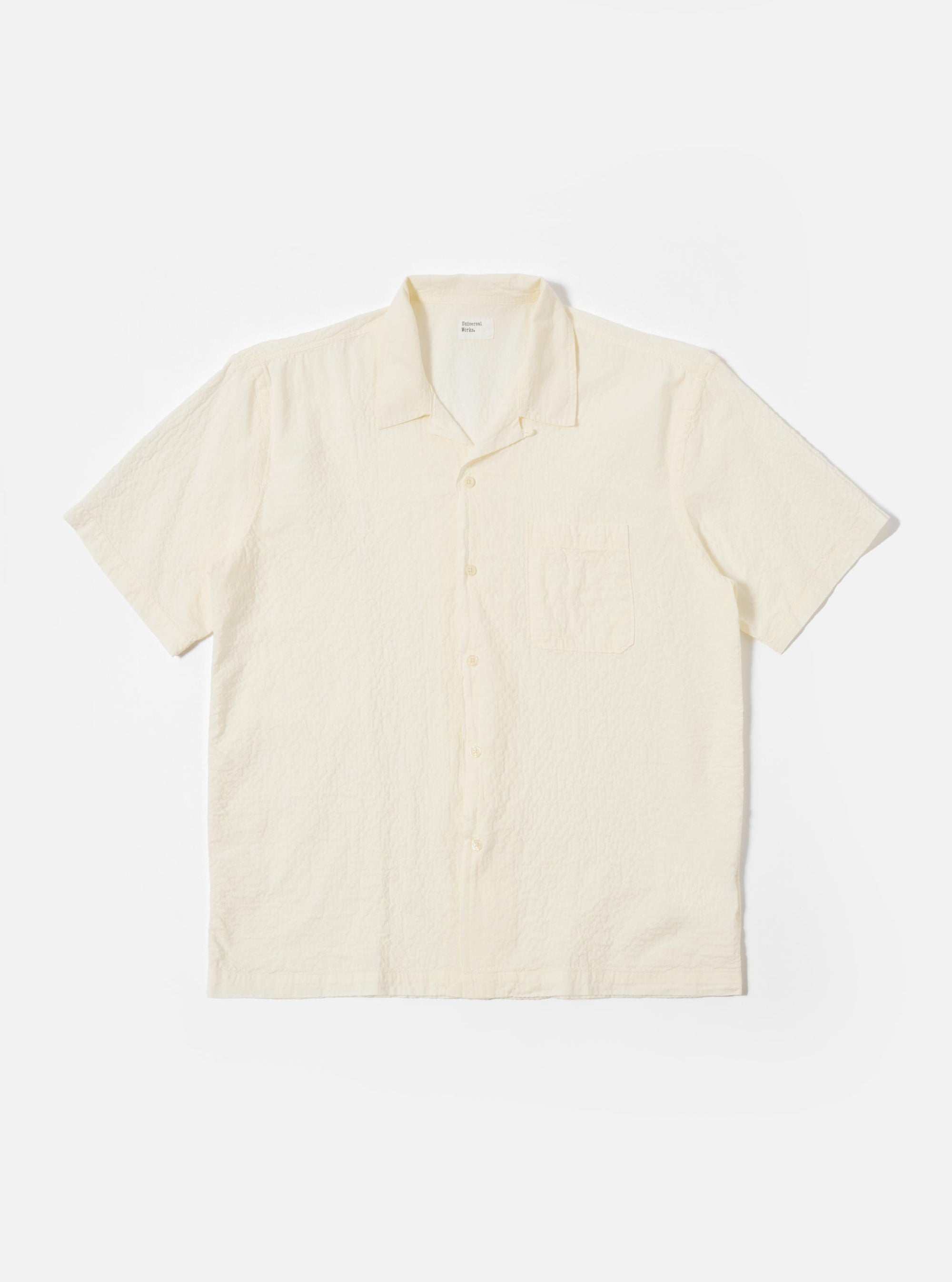 The Ecru Arten Seersucker Road Shirt is shown as a flat lay against a plain white background. The short-sleeve shirt features a camp collar with a loop-close button detail, a central button-down front, a single chest patch pocket, and a straight hem. The ecru-colored fabric has a distinct puckered seersucker texture.