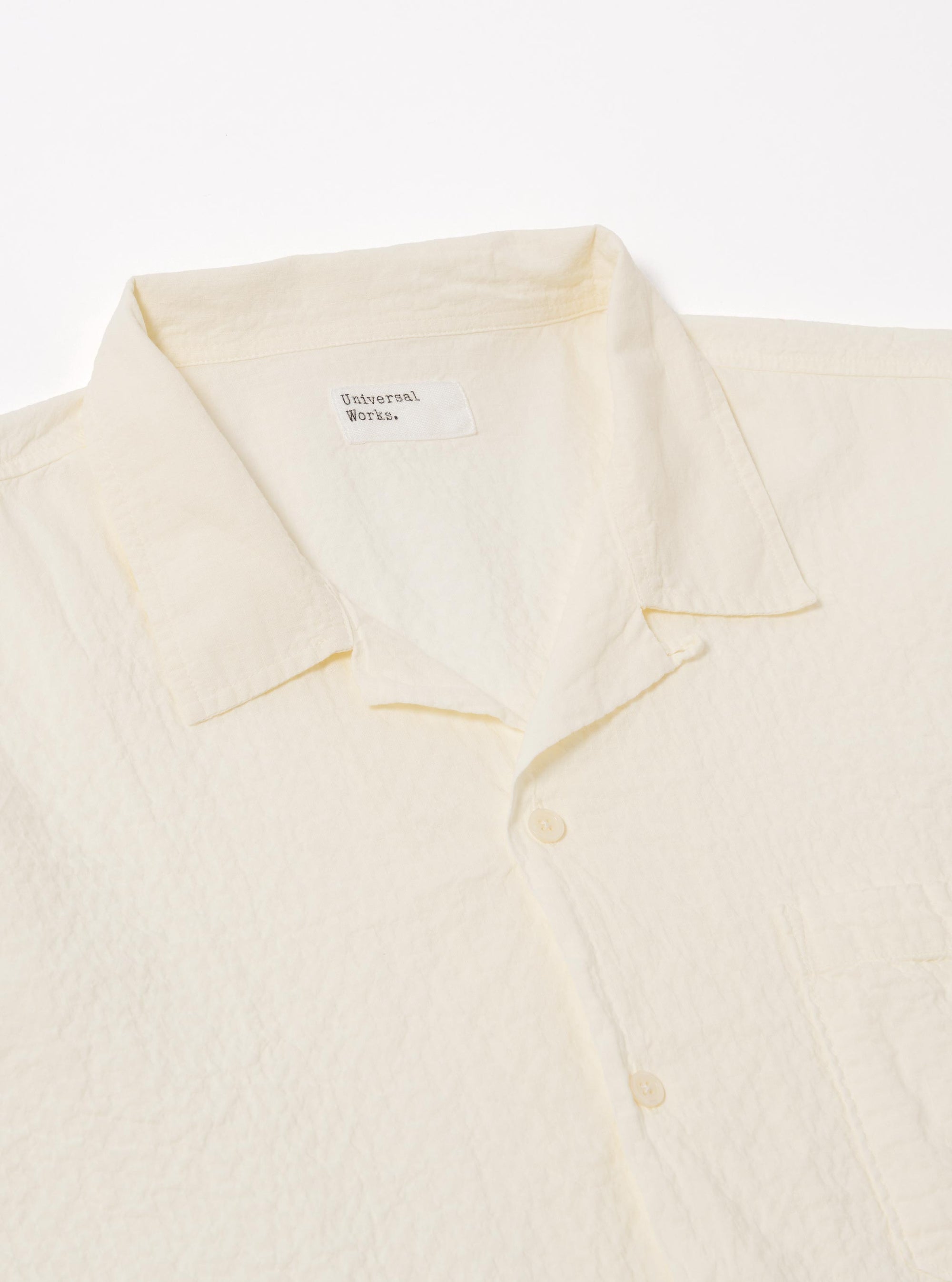 The Ecru Arten Seersucker Road Shirt is shown from the back as a flat lay against a plain white background. The image highlights the shirt's straight hem, short sleeves, and the distinct puckered texture of the ecru seersucker fabric.