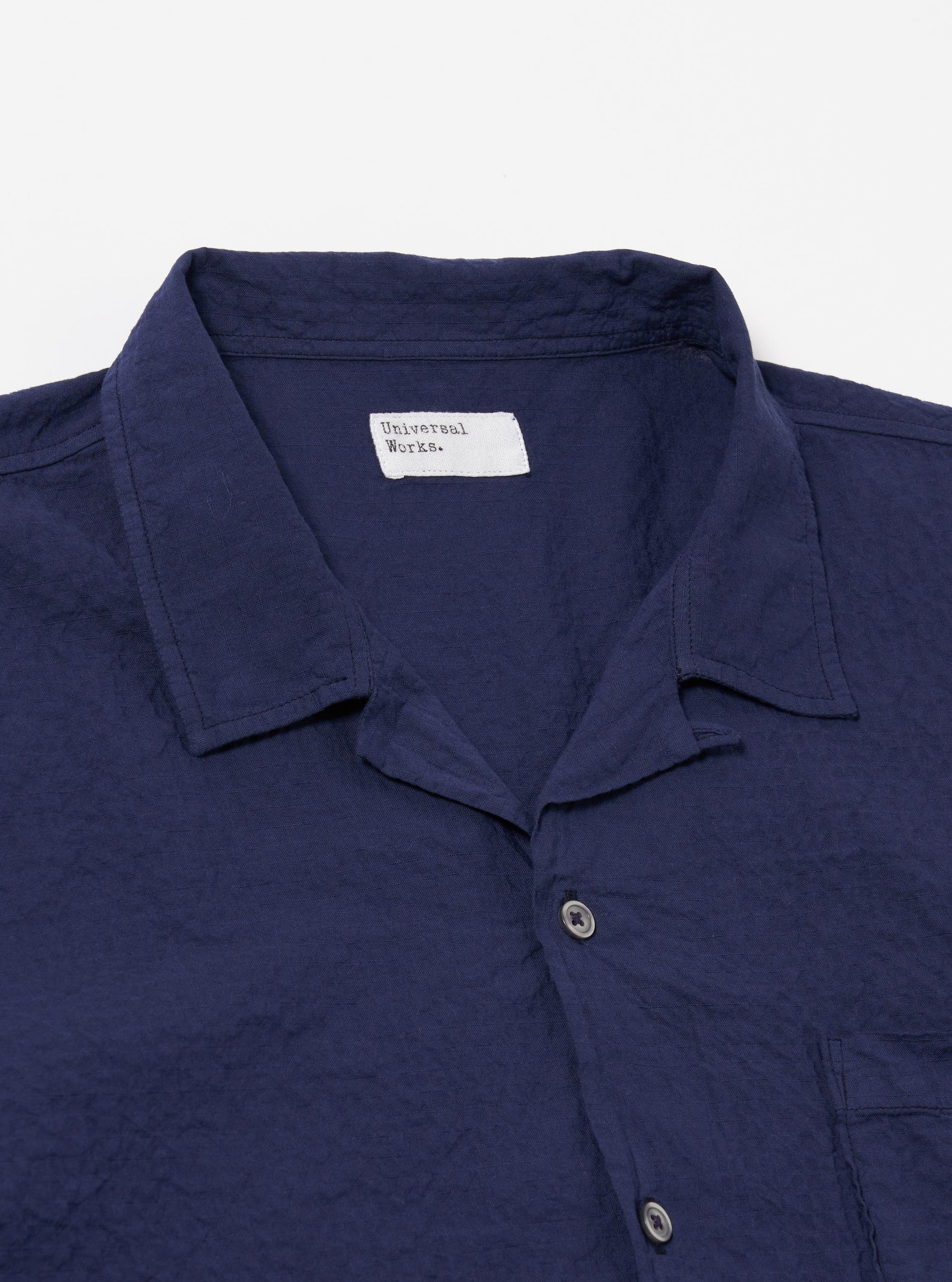 The Navy Arten Seersucker Road Shirt is shown from the back as a flat lay against a plain white background. The image highlights the garment's simple construction, featuring a straight hem, short sleeves, and a clean back panel. The navy blue organic cotton fabric exhibits a distinct puckered seersucker texture throughout.