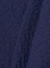A close-up fabric swatch of the Navy Arten Seersucker Road Shirt highlights the deep navy blue color and the distinct puckered texture of the organic cotton seersucker fabric. The material fills the frame, providing a detailed view of the garment's weave and color.