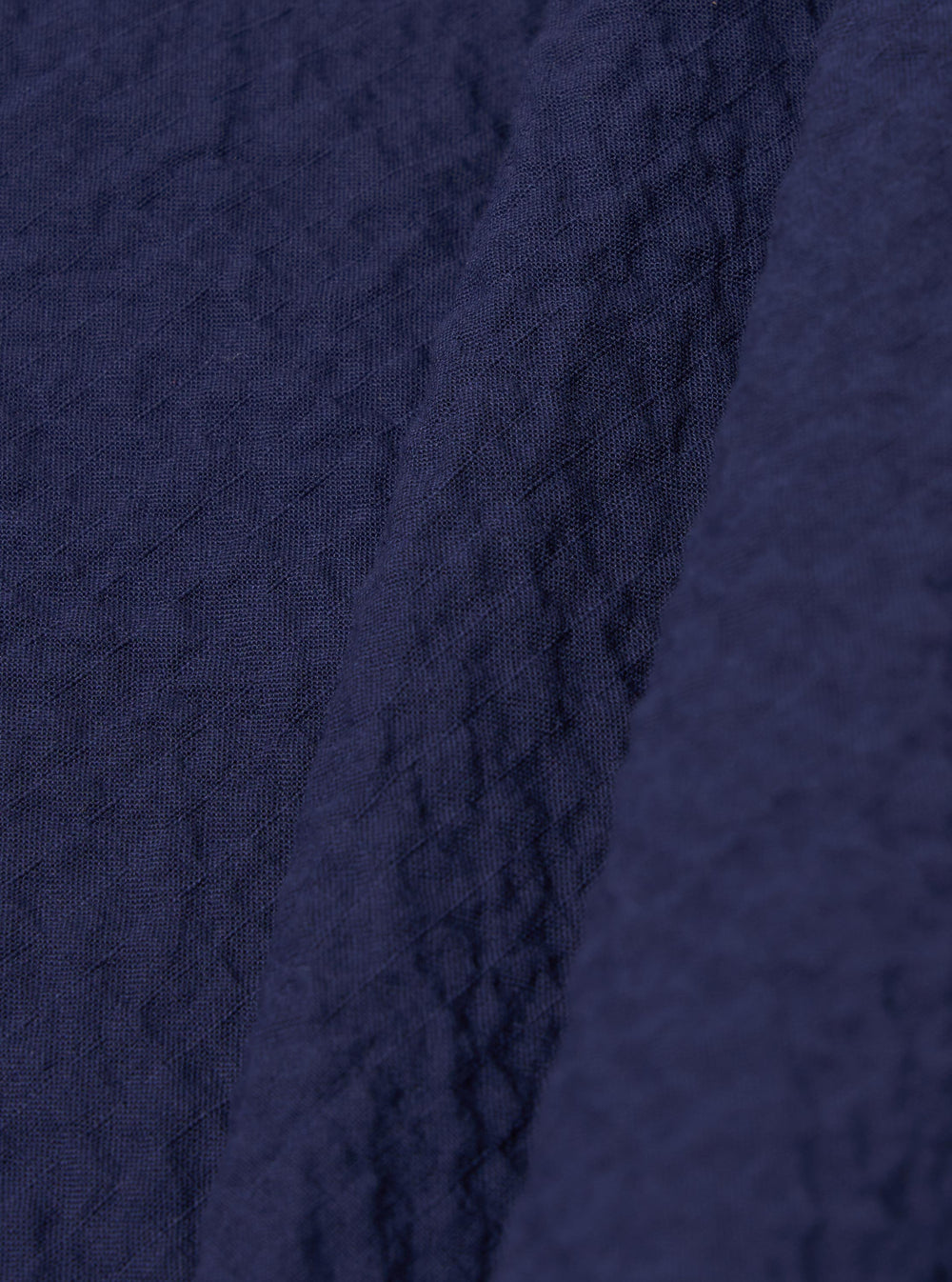 A close-up fabric swatch of the Navy Arten Seersucker Road Shirt highlights the deep navy blue color and the distinct puckered texture of the organic cotton seersucker fabric. The material fills the frame, providing a detailed view of the garment's weave and color.