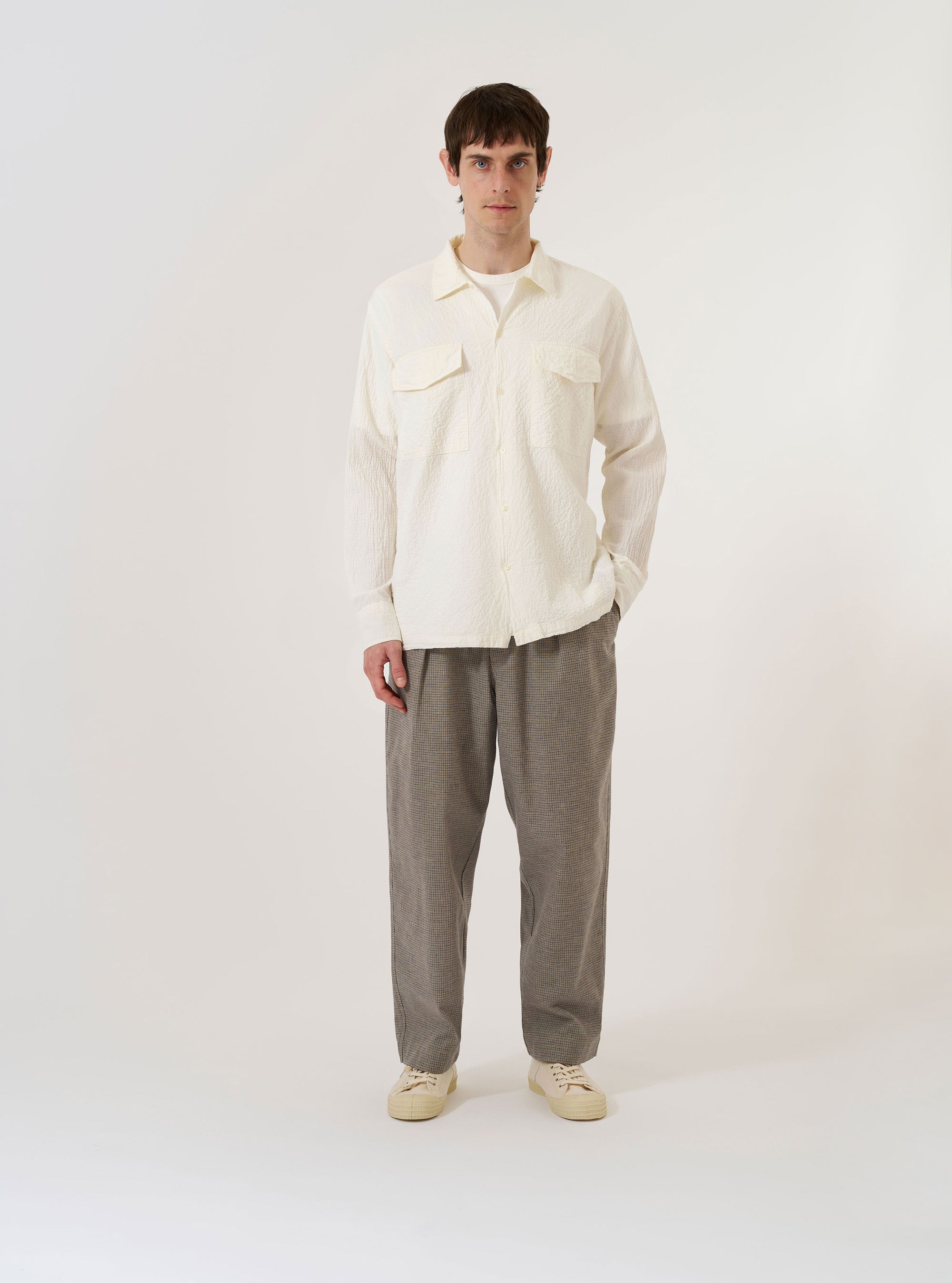 The Ecru Arten Seersucker Attendant Shirt is shown as a flat lay against a plain white background. The shirt features a central button-down front, a classic collar, and two large patch pockets at the waist. The ecru-colored organic cotton fabric has a distinct puckered seersucker texture.