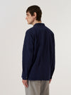 A model wears the Navy Arten Seersucker Attendant Shirt over a white t-shirt, shown from the rear three-quarter angle against a plain white background. The shirt features a loose fit, a straight hem, and a one-piece flat collar. The navy blue fabric has a distinct puckered seersucker texture.
