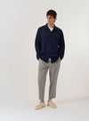 The Navy Arten Seersucker Attendant Shirt is displayed as a flat lay against a plain white background. This utility-style long-sleeve shirt features a flat one-piece collar, a central button-down front, and two oversized flap patch pockets on the chest. The navy organic cotton fabric has a distinct puckered seersucker texture.