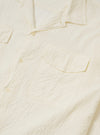 The Ecru Arten Seersucker Attendant Shirt is shown from the back as a flat lay against a plain white background. The image highlights the straight hem, two back pleated yokes, and the textured appearance of the ecru organic cotton seersucker fabric.