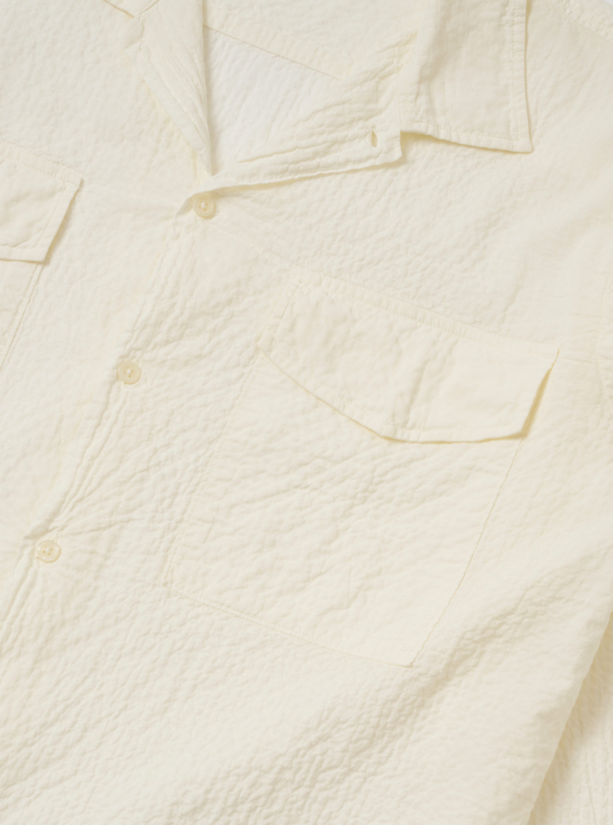 The Ecru Arten Seersucker Attendant Shirt is shown from the back as a flat lay against a plain white background. The image highlights the straight hem, two back pleated yokes, and the textured appearance of the ecru organic cotton seersucker fabric.