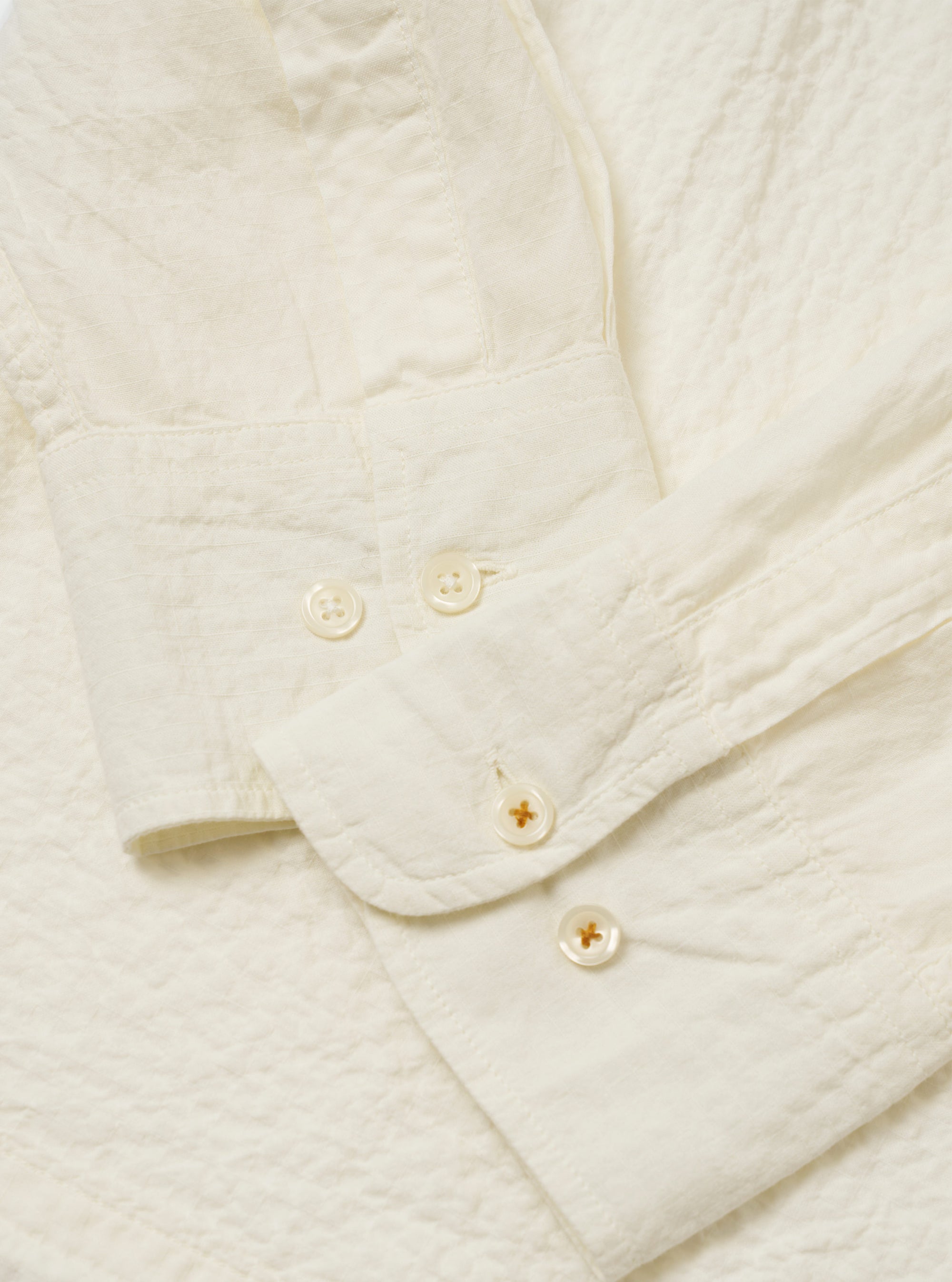 The Ecru Arten Seersucker Attendant Shirt is shown from the back in a flat lay against a plain white background. The image highlights the shirt's straight hem, simple back panel, and the puckered texture of the ecru seersucker fabric.