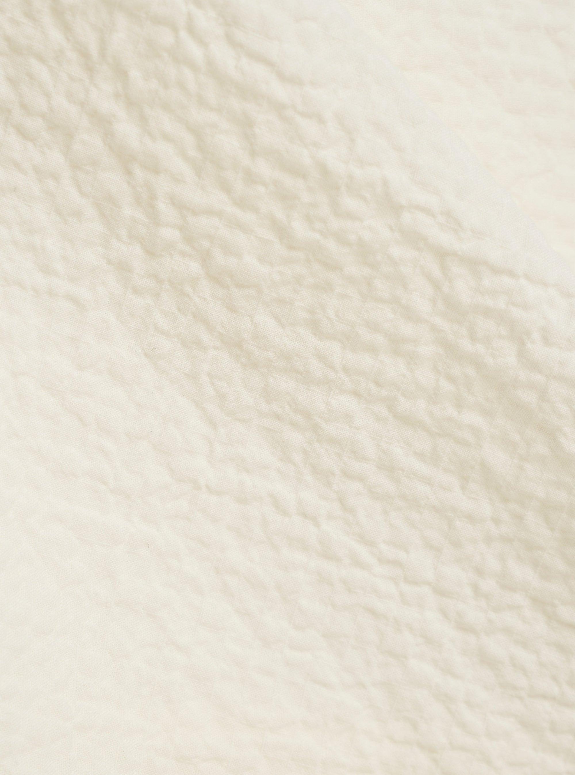 A close-up fabric swatch of the Ecru Arten Seersucker Attendant Shirt highlights the off-white color and the distinct puckered texture of the organic cotton seersucker fabric.