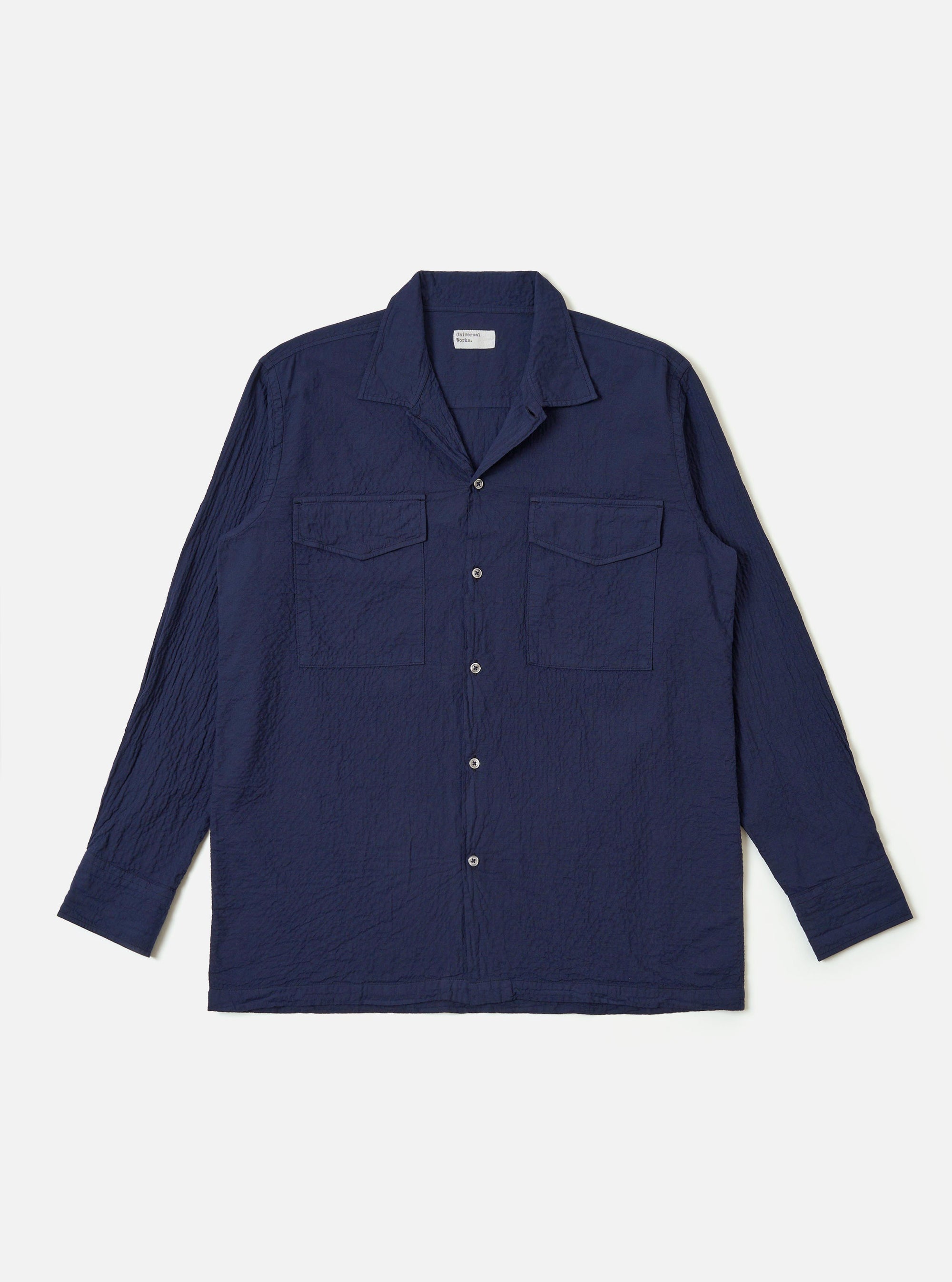 The Navy Arten Seersucker Attendant Shirt is shown as a flat lay against a white background. The shirt features a central button-down front, a classic collar, and two large patch pockets at the waist. The dark navy fabric has a distinct puckered seersucker texture.