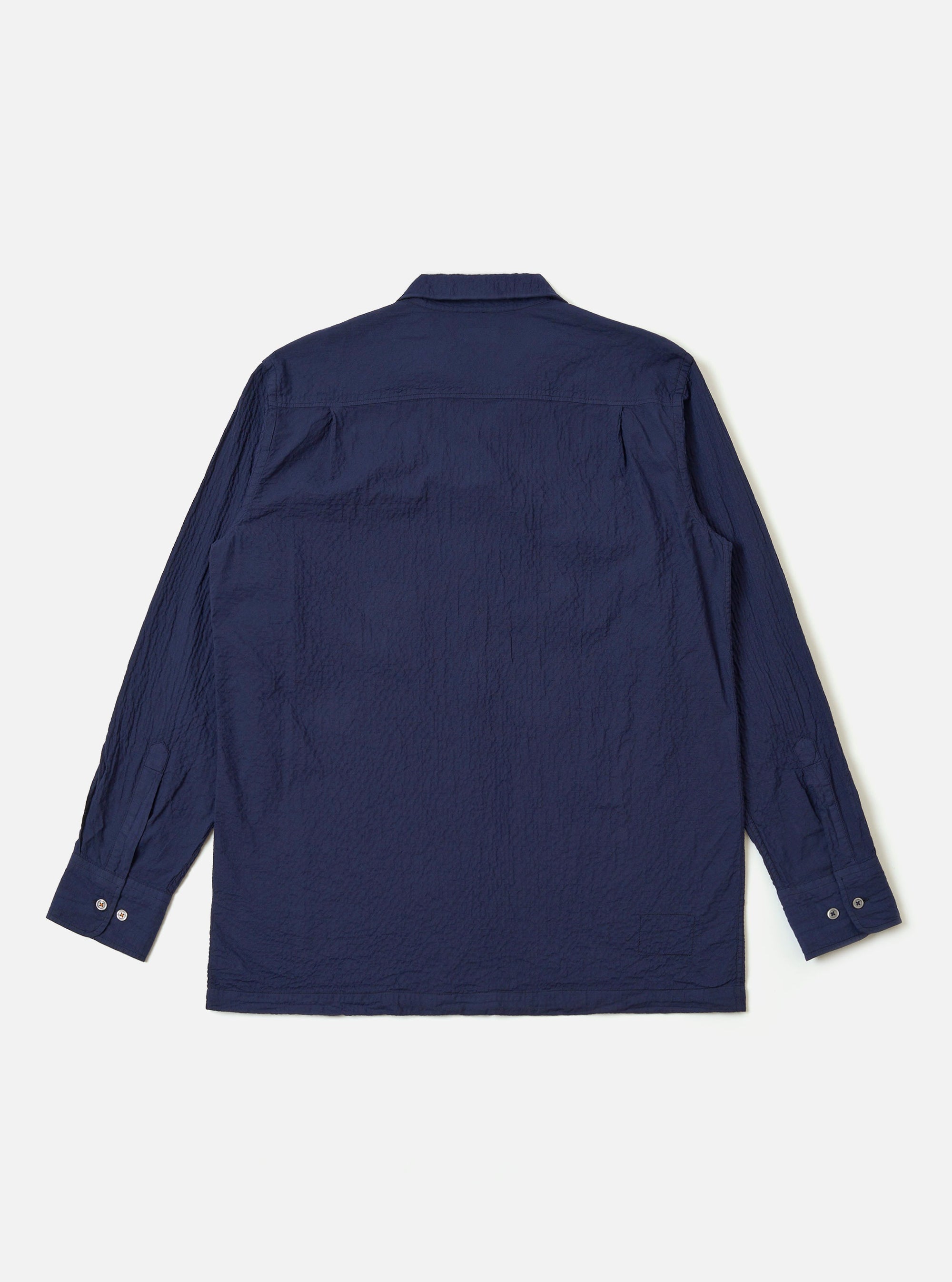 The Navy Arten Seersucker Attendant Shirt is shown from the back as a flat lay against a plain white background. The image highlights the shirt's clean, straight hem and simple back panel construction. The dark navy organic cotton fabric features a distinct and visible puckered seersucker texture throughout.