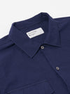 The Navy Arten Seersucker Attendant Shirt is shown from the back as a flat lay against a plain white background. The image highlights the shirt's straight hem, short sleeves, and the distinct puckered texture of the navy blue seersucker fabric. A simple yoke and a central vertical seam are visible on the rear panel.