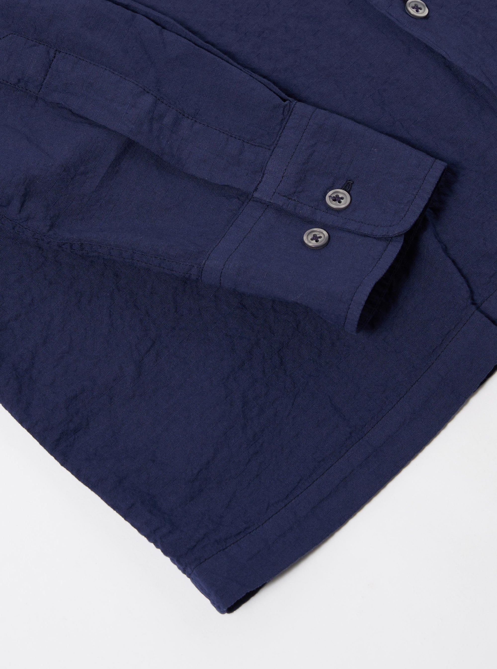 The Navy Arten Seersucker Attendant Shirt is shown from a rear three-quarter angle as a flat lay against a plain white background. The image highlights the shirt's straight hem, side vents, and the textured navy blue seersucker fabric with its characteristic puckered finish.