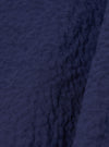 A close-up fabric swatch of the Navy Arten Seersucker Attendant Shirt highlights the deep navy blue color and the distinct puckered, crinkled texture of the organic cotton seersucker fabric. The material fills the entire frame, providing a detailed view of the textile's weave.