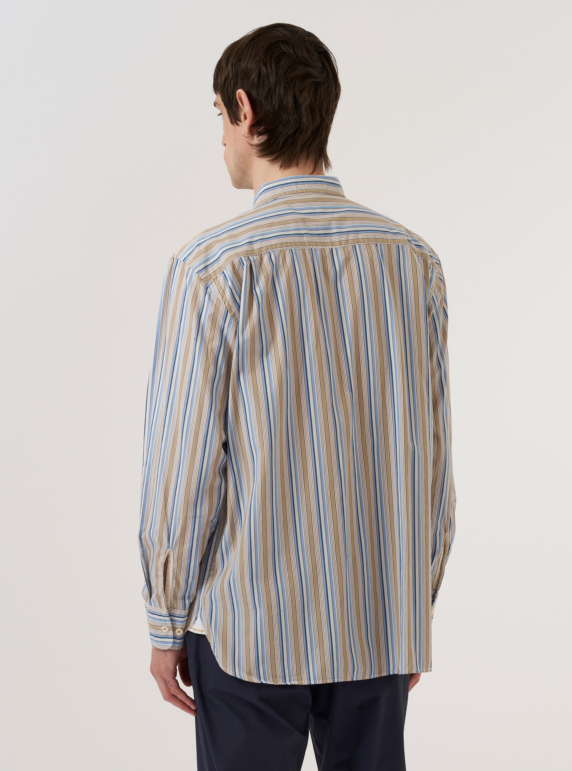 A model wears the Multi Pop Multi Stripe Square Pocket Shirt, shown from the back against a plain white background. The shirt features a bold vertical multi-stripe pattern in various colors throughout the fabric. The image highlights the straight-cut back panel and the continuation of the stripe design across the shoulders and sleeves. The model is shown from the waist up, emphasizing the garment's relaxed fit.