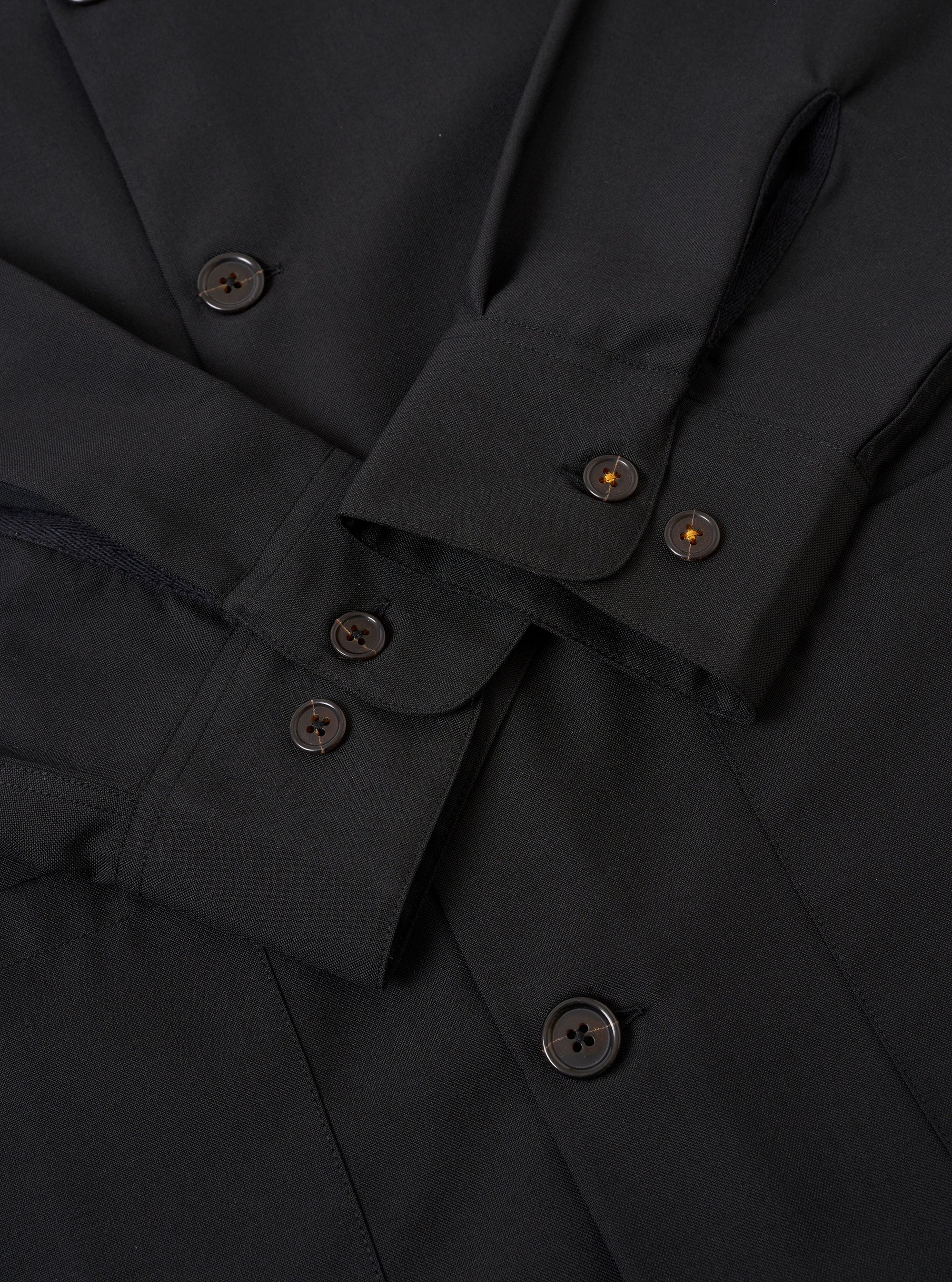 The Black Tropical Suiting Travail Overshirt is shown in a detail view as a flat lay against a plain white background. The image focuses on the lower front section of the garment, highlighting the smooth texture of the black tropical suiting fabric, the straight hem, and the clean stitching of a large patch pocket.