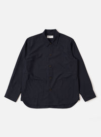 The Navy Tropical Suiting Travail Overshirt is shown as a flat lay against a white background. The garment features a single-piece collar, a button-through front, and two large patch pockets at the waist. It has adjustable button cuffs and a curved hem. The navy fabric is a lightweight tropical wool blend with a smooth, minimal appearance.