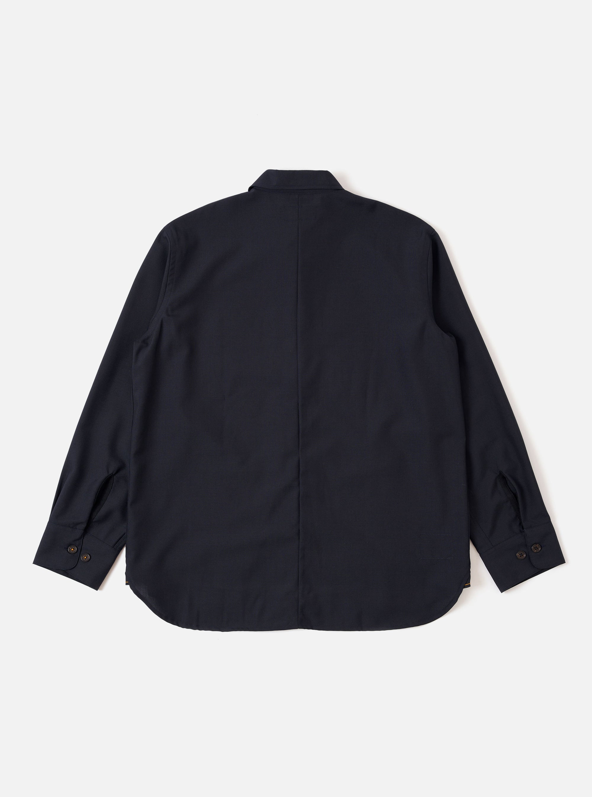 The Navy Tropical Suiting Travail Overshirt is shown from the back as a flat lay against a plain white background. The image highlights the clean construction of the garment's rear panel, featuring a simple one-piece collar, straight-cut yoke, and a curved hemline. The dark navy fabric has a smooth, lightweight tropical wool appearance.
