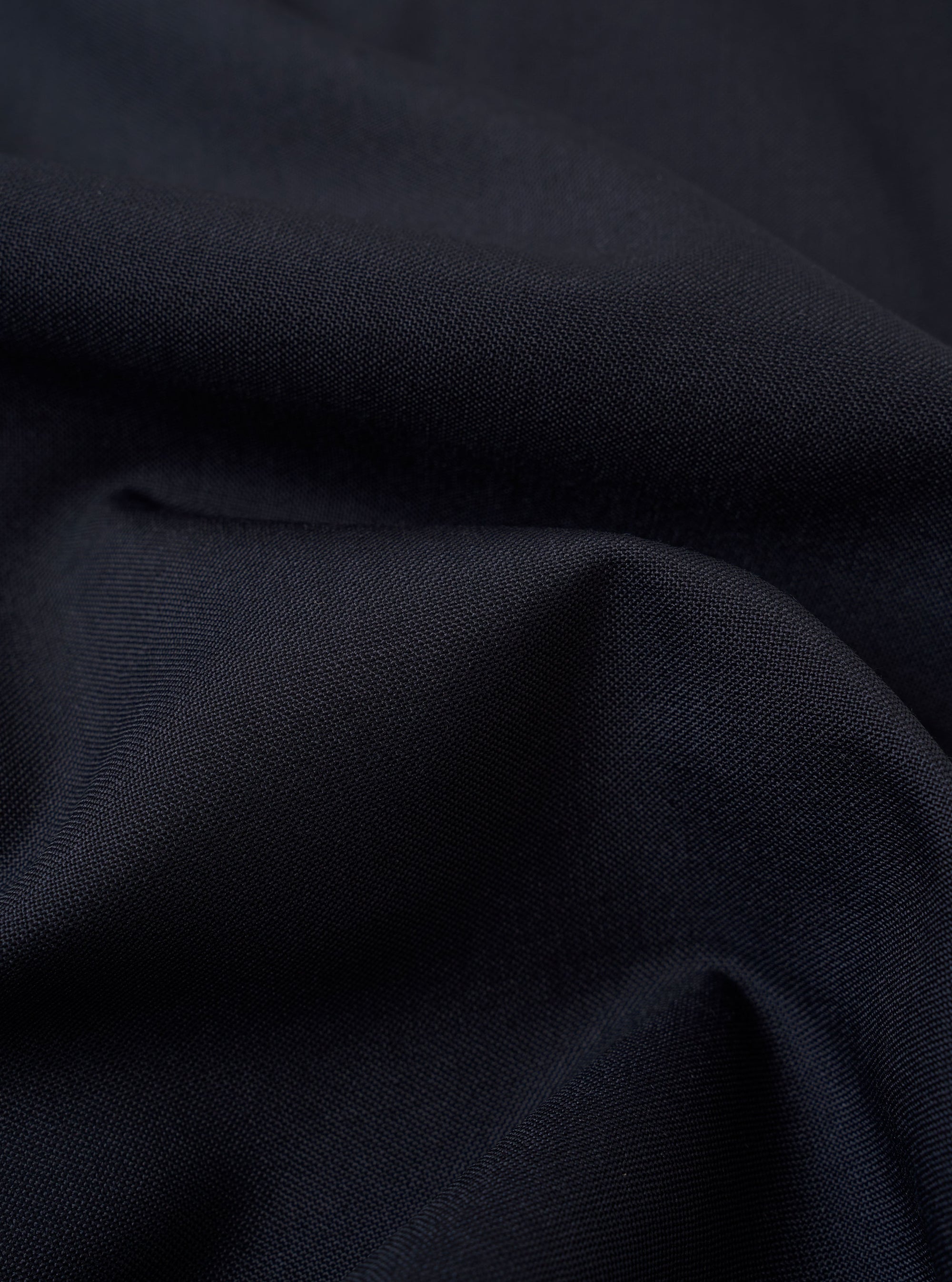 A close-up swatch image of the Navy Tropical Suiting Travail Overshirt fabric displays a deep navy blue color with a fine, smooth weave. The texture of the lightweight tropical wool and polyester blend is clearly visible, highlighting the professional suiting finish.