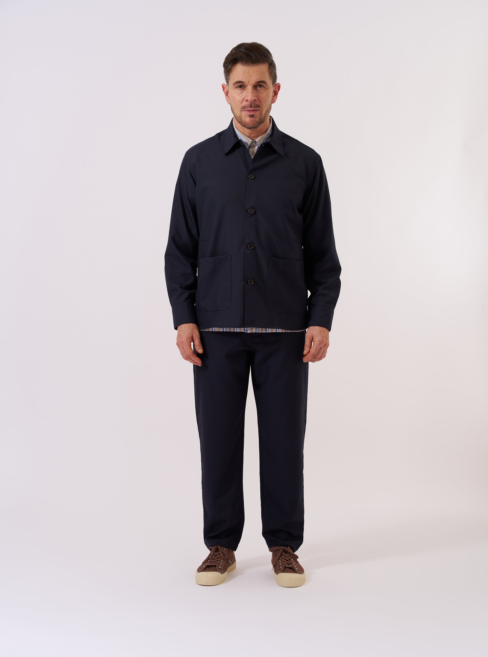The Navy Tropical Suiting Travail Overshirt is shown as a flat lay against a white background. The overshirt features a single-piece collar, a button-through front, and two large patch pockets at the waist. The navy blue tropical wool fabric has a smooth, lightweight appearance with a curved hem.