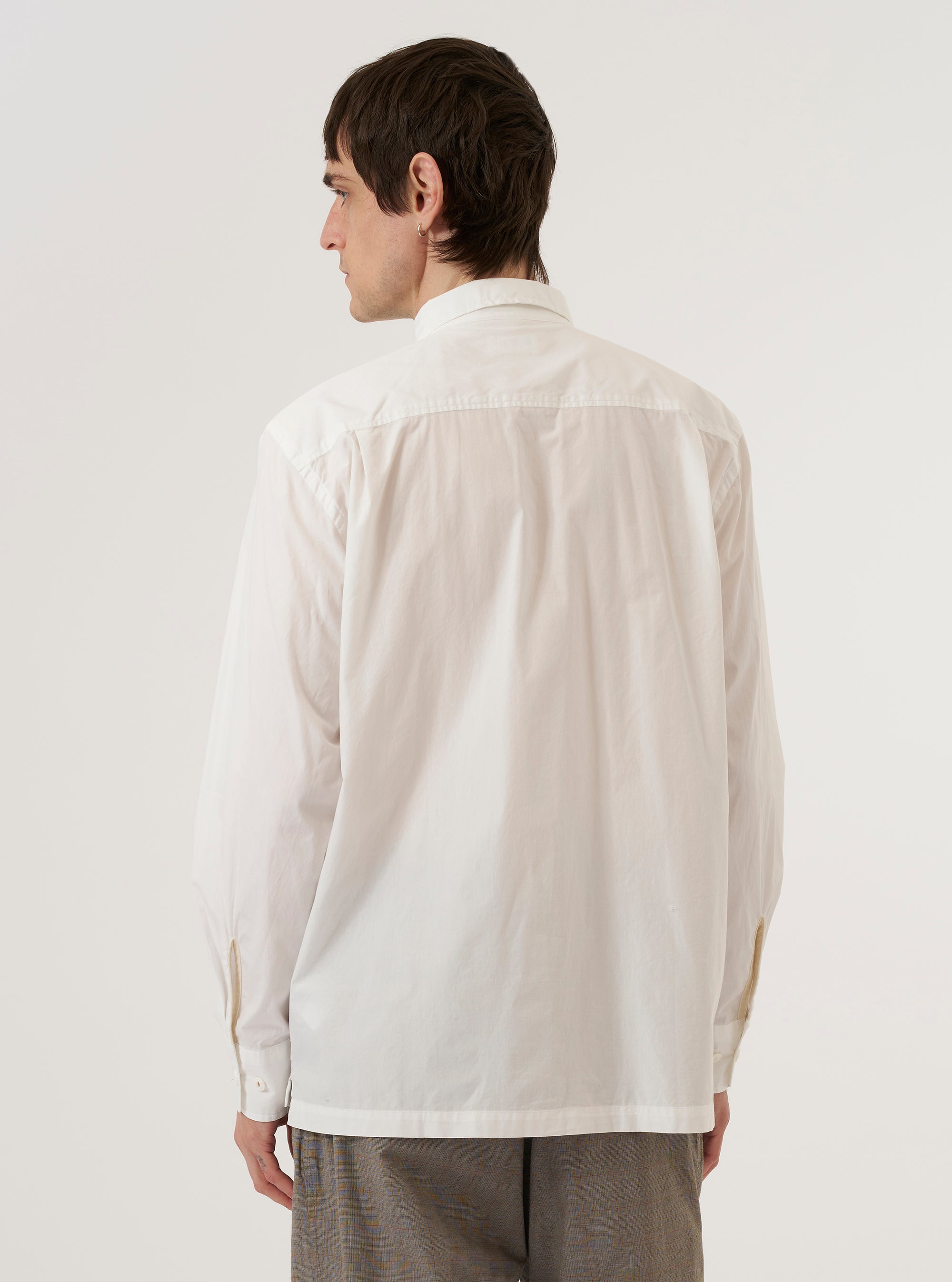 A model wears the Ecru Organic Fine Poplin CPO Shirt, shown from a rear three-quarter angle against a plain white background. The shirt features a clean back construction, a classic pointed collar, and a straight hem. The smooth, off-white ecru fabric of the organic fine poplin is clearly visible as the model stands facing away from the camera.