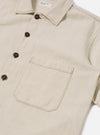The Ecru Koko Cotlin S/S Fatigue Shirt is shown in a detail view as a flat lay against a plain white background. The image highlights the textured ecru cotton-linen fabric and the construction of the functional front patch pockets and button-down closure.