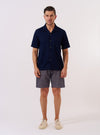 The Indigo Recycled Herringbone Road Shirt is shown as a flat lay against a white background. The shirt features a camp collar, a single chest patch pocket, and a straight hem. The indigo blue fabric has a visible herringbone weave pattern throughout.