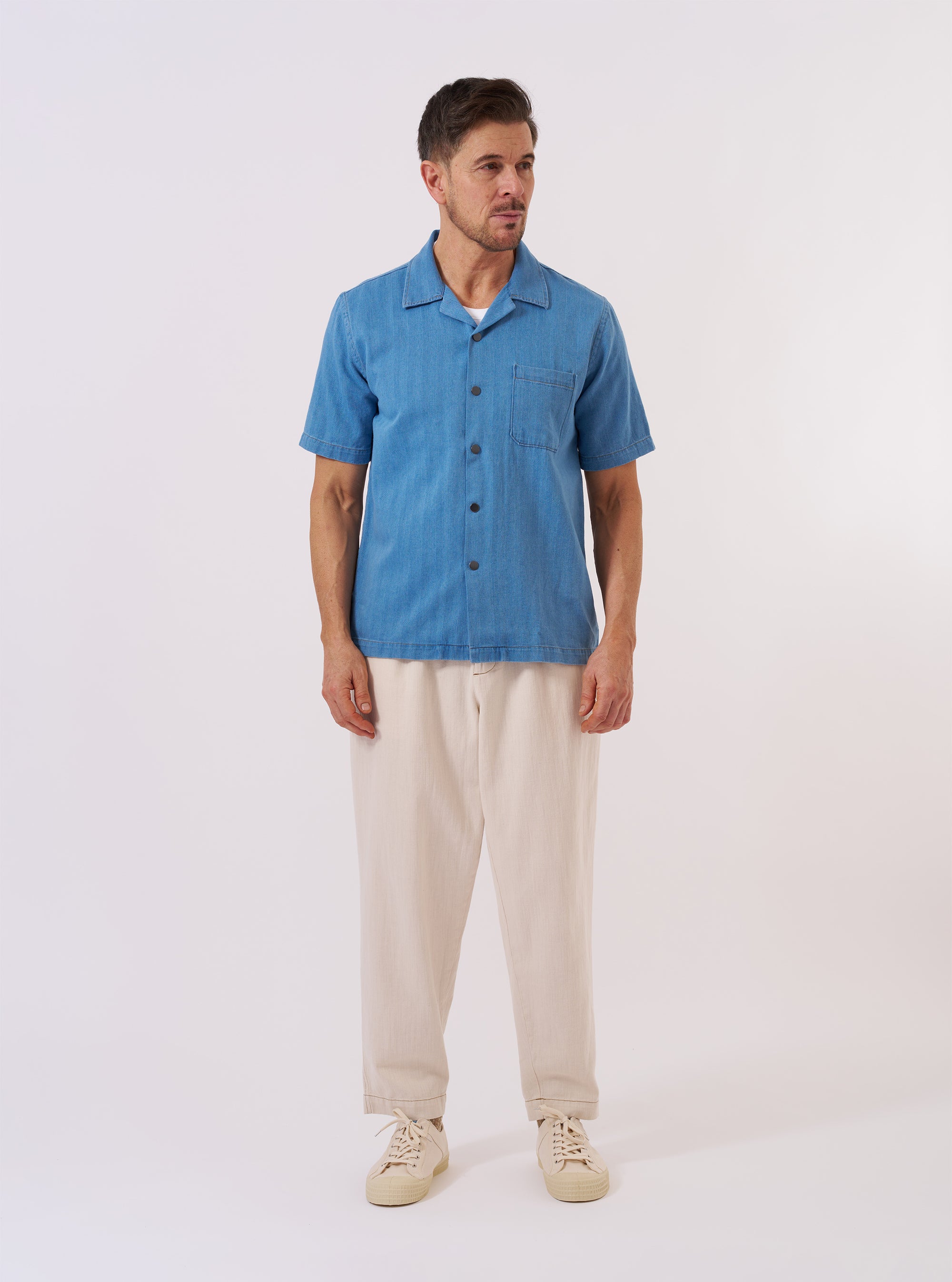 The Washed Indigo Recycled Herringbone Road Shirt is shown as a flat lay against a white background. The shirt features a camp collar, a six-button front closure, and two large chest patch pockets with button-down flaps. The fabric has a visible blue and white herringbone texture throughout.