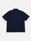 The Indigo Recycled Herringbone Road Shirt is shown from the back as a flat lay against a white background. The shirt features two back pleats for ease of movement and a straight hem. The indigo-dyed fabric displays a visible herringbone weave pattern throughout.