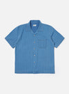 The Washed Indigo Recycled Herringbone Road Shirt is shown as a flat lay against a plain white background. The shirt features a camp collar, a six-button front closure, and two large chest pockets with button-down flaps. The fabric is a washed indigo blue with a visible herringbone weave.