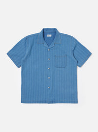 The Washed Indigo Recycled Herringbone Road Shirt is shown as a flat lay against a plain white background. The shirt features a camp collar, a six-button front closure, and two large chest pockets with button-down flaps. The fabric is a washed indigo blue with a visible herringbone weave.