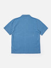 The Washed Indigo Recycled Herringbone Road Shirt is shown from the back as a flat lay against a plain white background. The image highlights the shirt's straight hem, simple collar, and the subtle chevron texture of the washed indigo herringbone fabric.