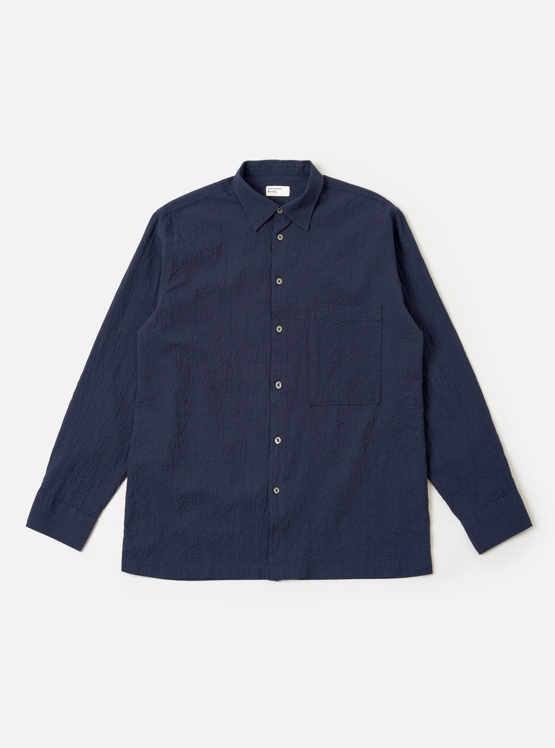 The Navy Seersucker Shirting Lucky Shirt is shown as a flat lay against a plain white background. The shirt features a central button-down front, a single patch pocket on the left chest, and a classic pointed collar. The fabric has a distinct puckered seersucker texture in a deep navy blue.