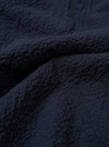 A close-up fabric swatch of the Navy Seersucker Shirting Lucky Shirt highlights the deep navy blue color and the distinct puckered texture of the seersucker material. The image provides a detailed view of the cotton fabric's weave and consistent tone.