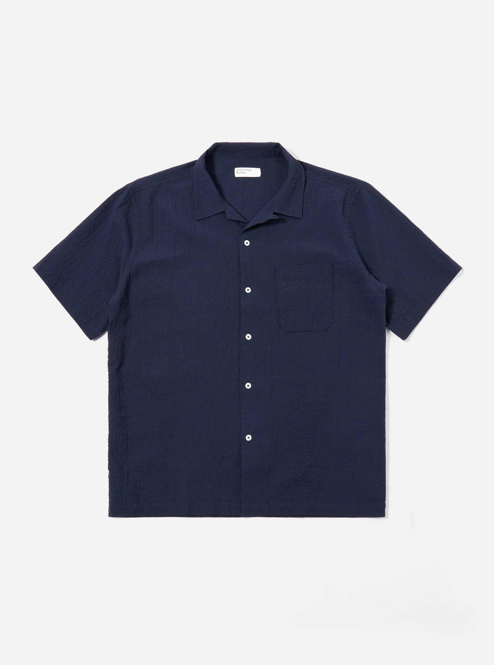 The Navy Seersucker Shirting Road Shirt is shown as a flat lay against a plain white background. The shirt features a camp collar, a central button-down front with tonal buttons, a single chest patch pocket, and short sleeves. The dark navy fabric has a distinct puckered seersucker texture.