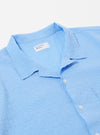 The Sky Blue Seersucker Shirting Road Shirt is shown from the back as a flat lay against a plain white background. The image highlights the shirt's straight hem, short sleeves, and the puckered texture of the sky blue seersucker fabric. A horizontal yoke across the shoulders and a small white brand label near the hem are visible.