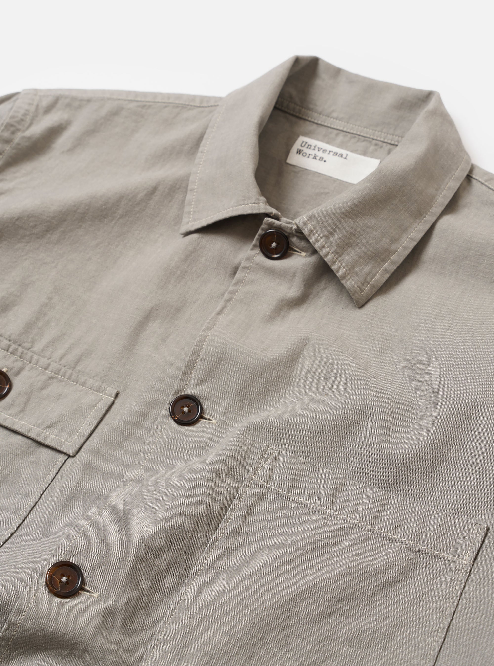 The Grey Izumi Cotton Dockside is shown from the back as a flat lay against a plain white background. The garment features a straight hem, a simple yoke across the shoulders, and a relaxed fit. The fabric has a subtle textured appearance in a solid grey color.