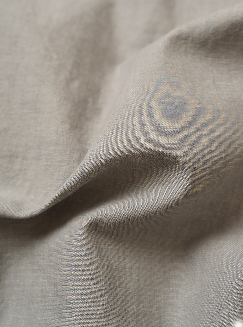 The Grey Izumi Cotton Dockside is shown from the back as a flat lay against a white background. The image highlights the back yoke with small pleats and the relaxed, boxy fit of the overshirt. The lightweight cotton fabric features a visible marled texture with slubbed threads.