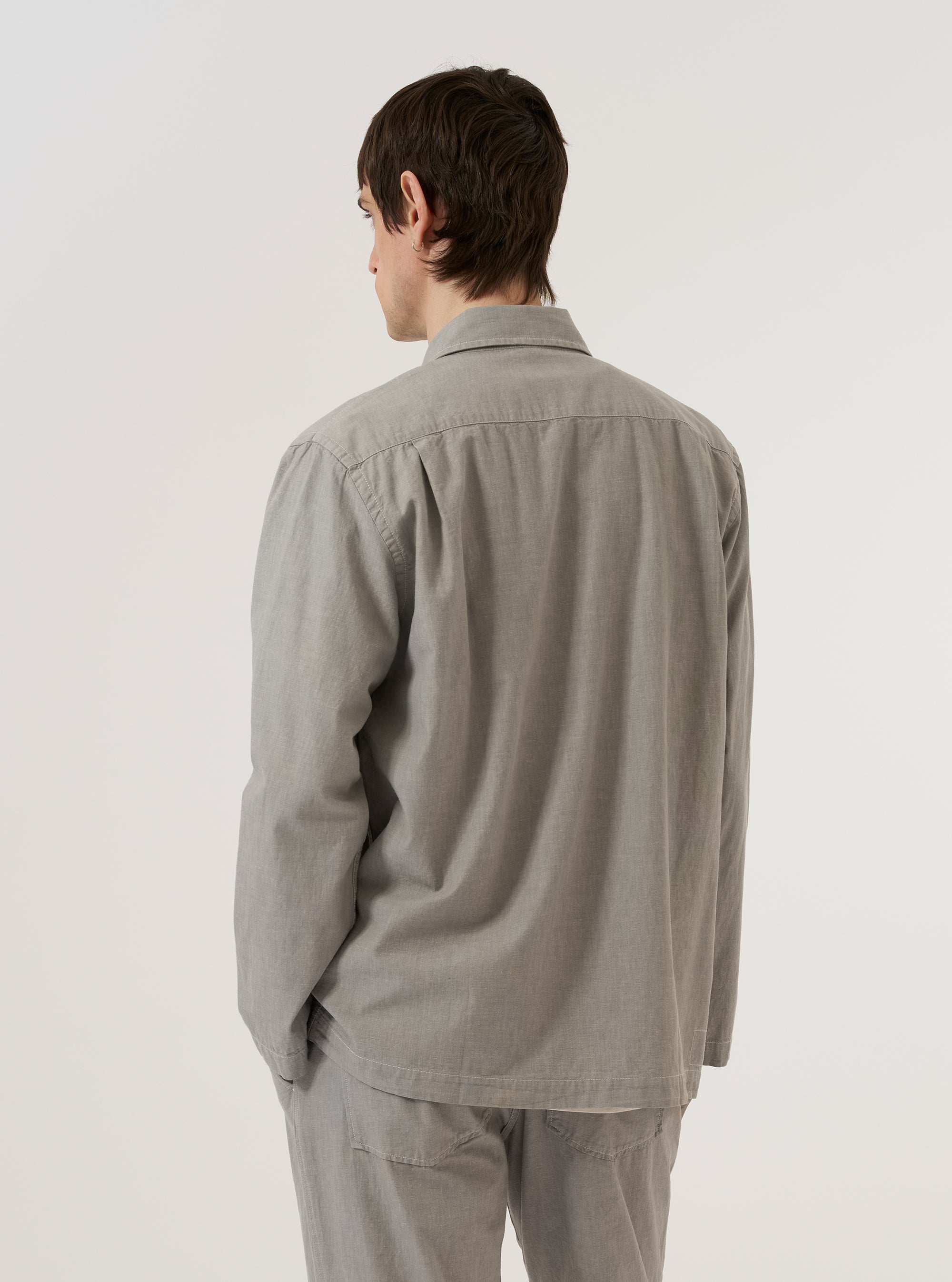 A model is wearing the Grey Izumi Cotton Dockside, shown from the back against a plain white background. The overshirt features a relaxed fit, a straight hem, and a simple back panel. The grey Izumi cotton fabric has a distinct textured appearance. No mannequin is present in the image.