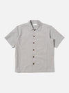 The Grey Izumi Cotton S/S Fatigue Shirt is shown as a flat lay against a white background. The shirt features a classic collar, a central button-down closure, and short sleeves. Two large patch pockets with button flaps are prominent on the chest. The fabric is a solid grey cotton with a smooth texture.