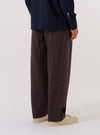 A model wears the Brown Chester Stripe Oxford Pant, shown from a rear angle against a plain white background. The trousers feature a loose, wide-leg fit and an all-over vertical brown stripe pattern. The garment is styled with a relaxed silhouette, highlighting the drape of the cotton fabric and the elasticated waistband.