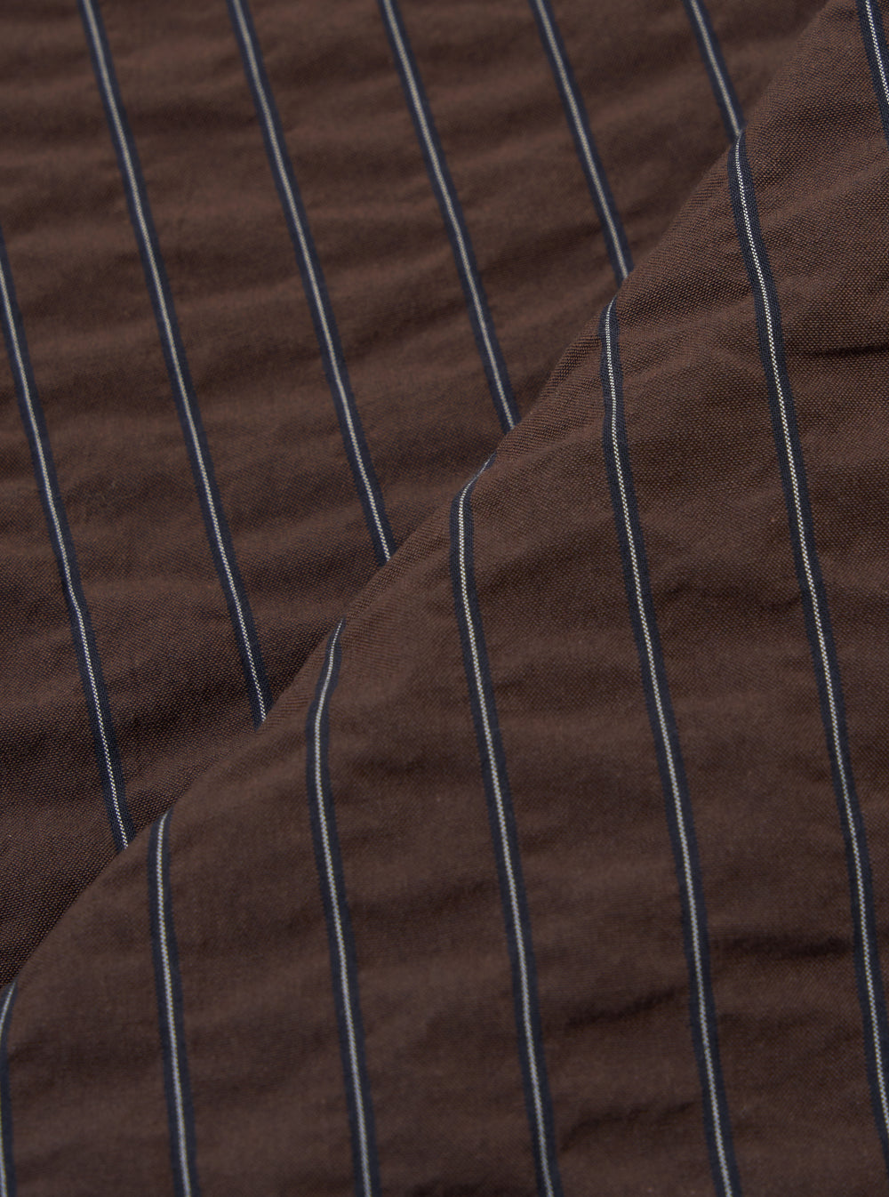 A close-up fabric swatch of the Brown Chester Stripe Two Button Jacket highlights the brown color and the distinct vertical stripe pattern. The image provides a detailed view of the material's texture and weave.