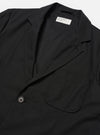 The Black Valencia Cotton Two Button Jacket is worn by a model against a plain white background. The image shows a rear three-quarter view, highlighting the jacket's loose fit, structured shoulders, and central back seam. The black fabric has a smooth finish, and the model is wearing the jacket over a light-colored long-sleeve top. No mannequin is present in the image.