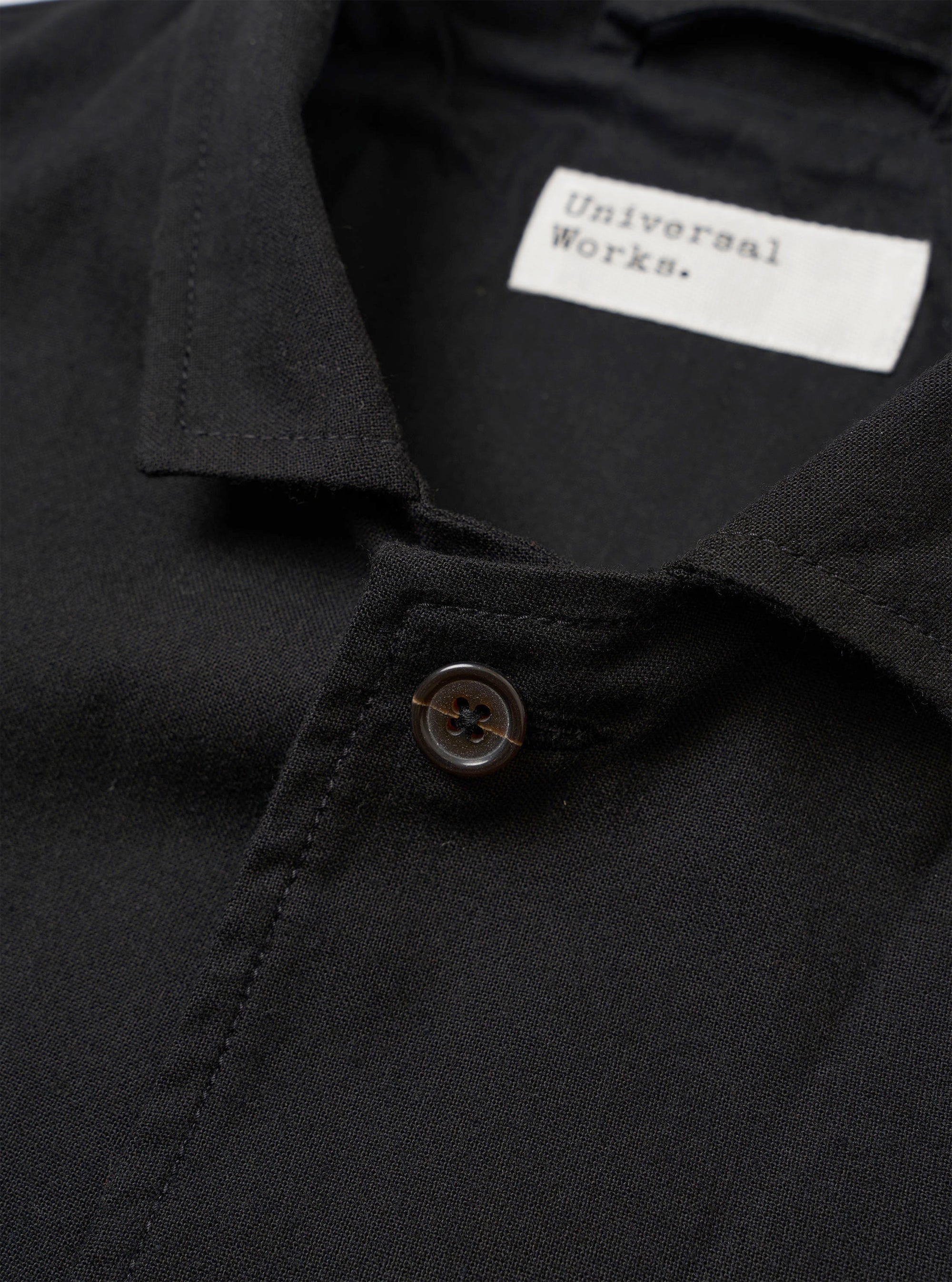 The Black Valencia Cotton Two Button Jacket is shown from the back as a flat lay against a plain white background. The image highlights the garment's rear construction, featuring a central vertical seam and a clean, straight hem. The black fabric appears smooth with a subtle technical finish.