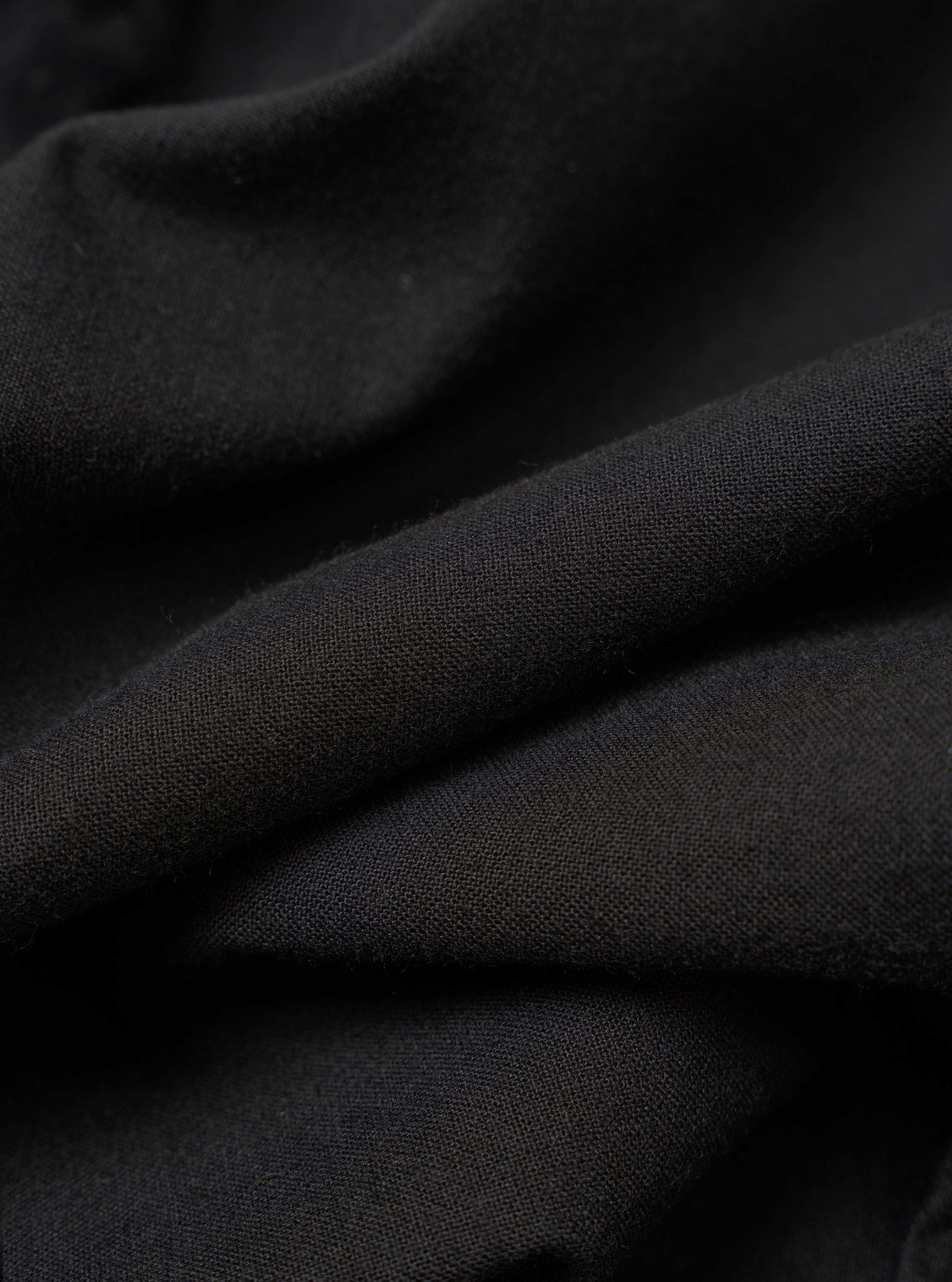 The Black Valencia Cotton Two Button Jacket is shown in a detail view as a flat lay against a plain white background. The image highlights the textured weave of the black cotton-blend fabric and the construction of the lower front patch pocket.