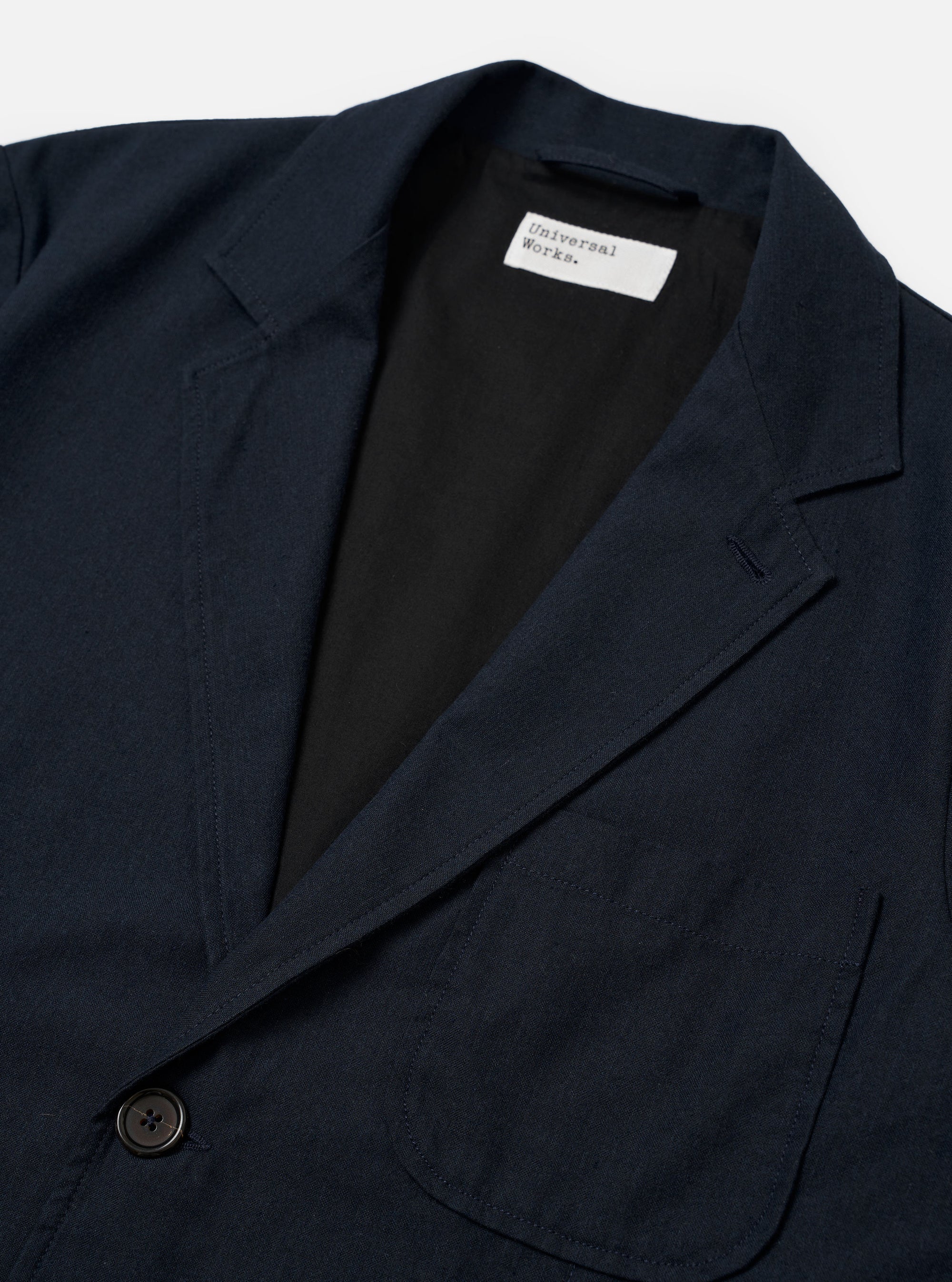 The Navy Valencia Cotton Two Button Jacket is shown from the back as a flat lay against a plain white background. The image highlights the clean construction of the rear panel and the textured navy blue cotton-blend fabric. The jacket features two vents at the hem and visible stitching along the seams and shoulders.